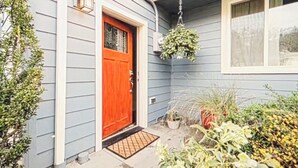 Ein Haus mit roter Tür, einem hängenden Blumentopf und verschiedenen Kübelpflanzen.