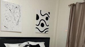 Ein ordentlich bezogenes Bett mit weißer und schwarzer Bettwäsche, ein schwarzer Kopfteil und ein abstraktes Schwarz-Weiß-Gemälde an der Wand.