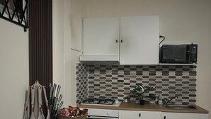 Eine Küche mit weißen Schränken, einer Mikrowelle, einem Gasherd und einer gefliesten Spritzschutzwand. Auf der Arbeitsplatte liegt ein Schild und ein Korb mit Snacks.