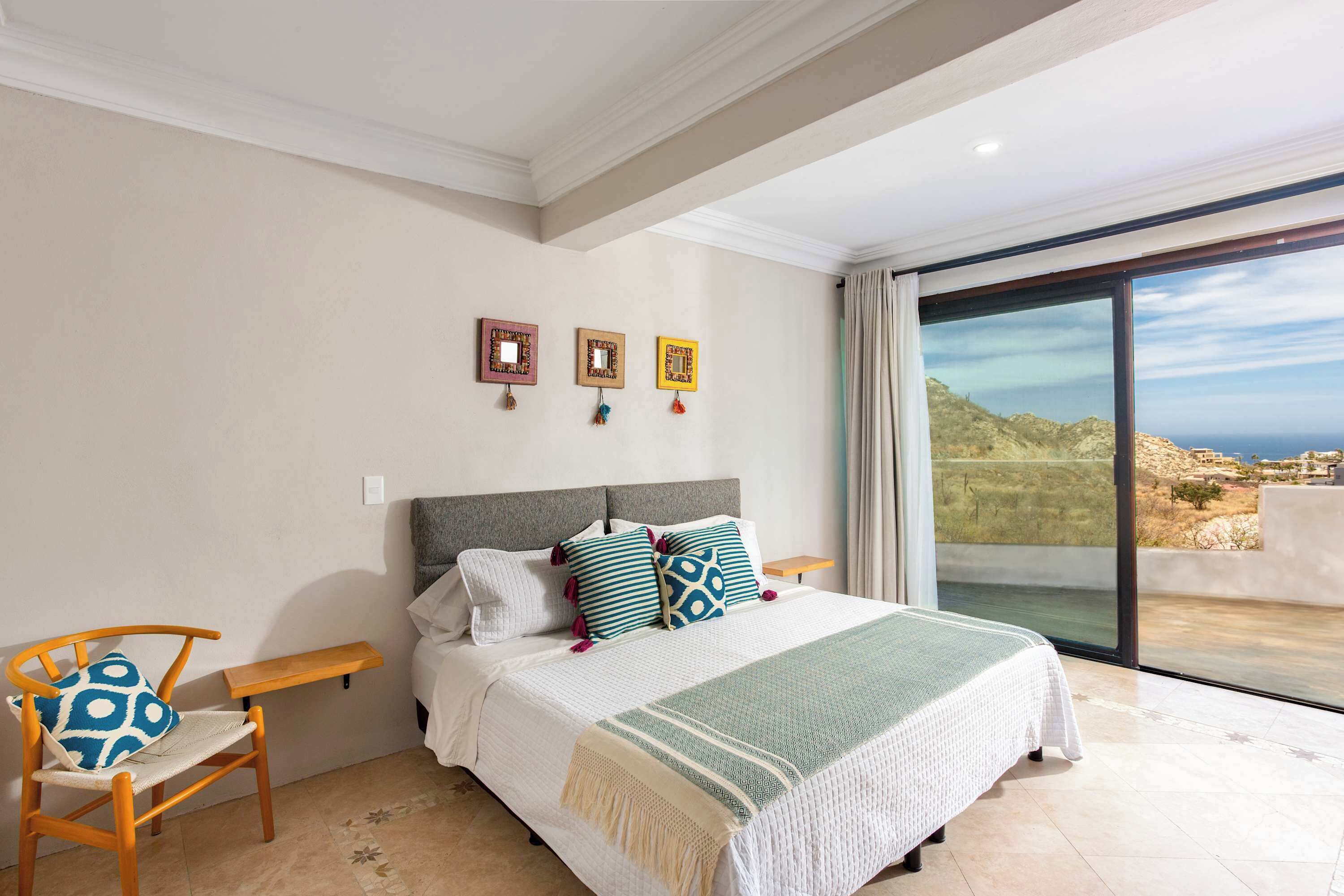 Une chambre à coucher avec un lit, une chaise, une petite table et une vue sur la mer par une grande fenêtre.