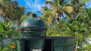 A green outdoor grill with a dome lid, set on a cart, surrounded by palm trees and a clear blue sky. - Walk to the Beach (Sarasota)