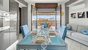 Een moderne eetruimte met een glazen tafel, blauwe stoelen en een uitzicht op de stad door grote glazen deuren.