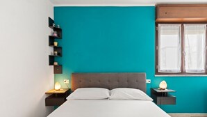 Een moderne slaapkamer met een turquoise accentmuur, een gestoffeerd hoofdeinde, een bed met witte lakens en twee nachtkastjes met lampen.