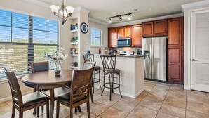 A modern kitchen with wooden cabinets, stainless steel appliances, and a dining area with a round table and chairs. - Close To Disney, Clubhouse With Gym, Communal Pool (Davenport)