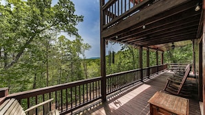 Une terrasse en bois, agrémentée de bancs et de tables, entourée d’arbres.