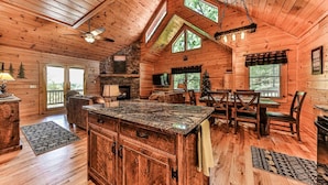 Un intérieur spacieux de chalet en bois, avec un grand îlot de cuisine, un coin repas et une cheminée.