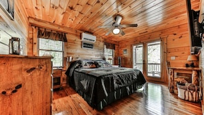 Une chambre dans une cabane en bois, avec un lit, un ventilateur de plafond et une fenêtre.