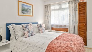 A bedroom with a bed, a nightstand, a window with curtains, and a door. - Beachside - Sea Views Village Centre Saundersfoot (Saundersfoot)