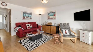A living room with a red sofa, a zebra-patterned rug, a wooden coffee table, a patterned armchair, and a white dresser with a flat-screen TV mounted above it. - Beachside - Sea Views Village Centre Saundersfoot (Saundersfoot)