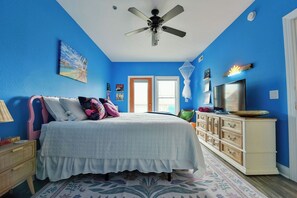 Une chambre à coucher comprenant un lit, un ventilateur de plafond, une commode et un téléviseur.