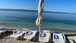 Une plage à l’eau cristalline, une rangée de chaises longues blanches et un seul parasol.