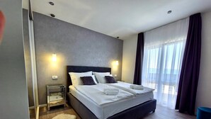 Une chambre d’hôtel moderne avec un grand lit, une table de chevet, un tapis moelleux et une vue sur l’extérieur grâce à de grandes fenêtres.