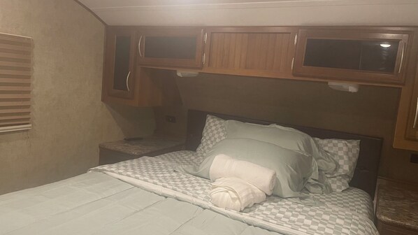 A bedroom with a bed, a nightstand, and wooden cabinets above the bed.