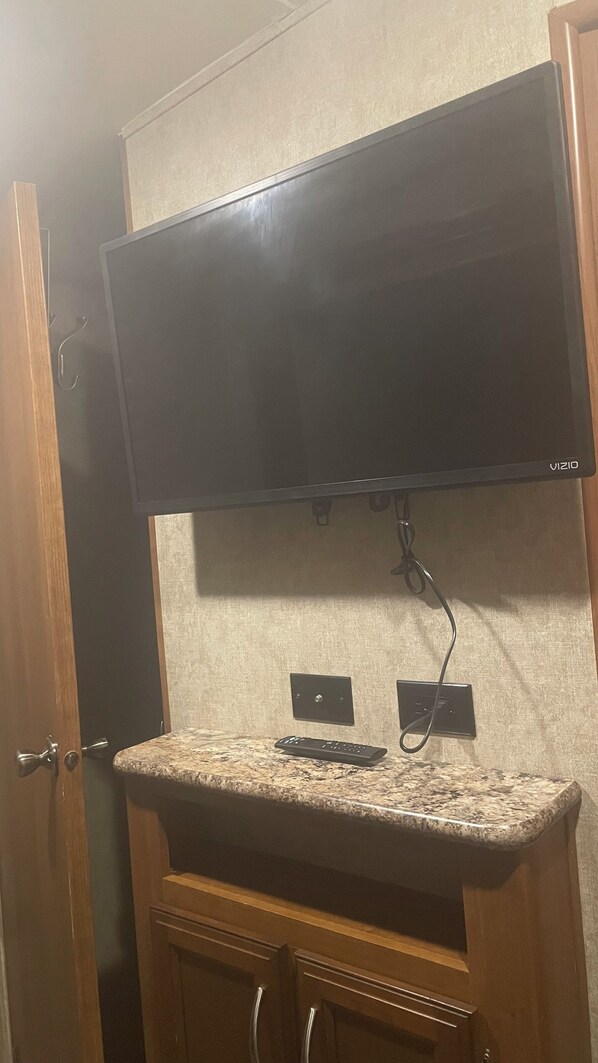 A kitchen with a granite countertop, a black remote control, and a flat-screen TV mounted above the counter. - Cozy 2-bedroom RV in excellent Valrico/Tampa with WiFi, AC, Heat, Hot water (Valrico)
