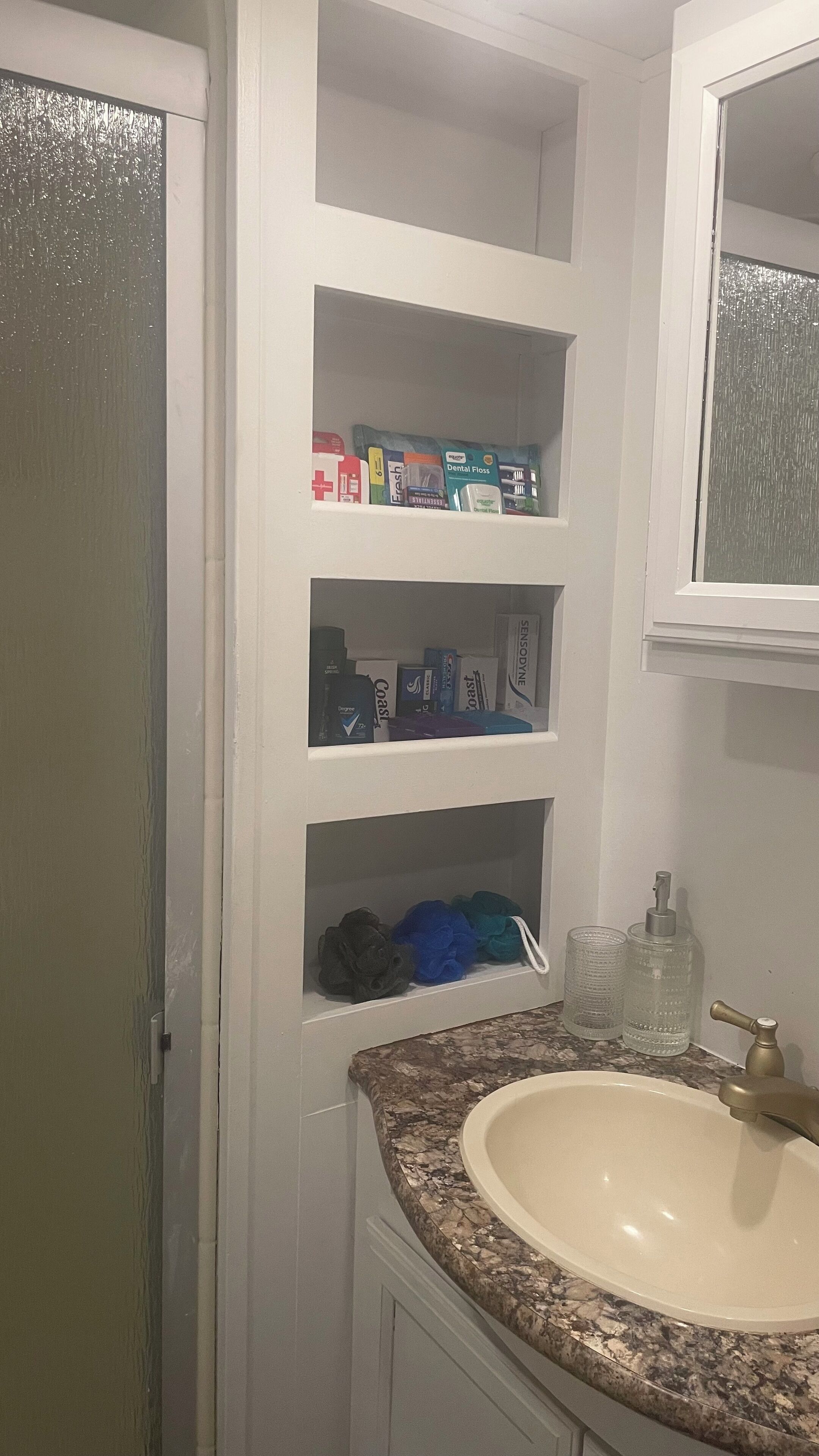 A bathroom with a white vanity, a sink, and shelves containing toiletries.