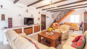 A living room with a sofa, coffee table, and a TV. There is a staircase leading to another level. - Finca Meraki Ojén by Ruralidays (Málaga)