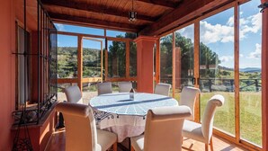 A sunlit room with a round table and chairs, large windows with a view of a hilly landscape. - Finca Meraki Ojén by Ruralidays (Málaga)