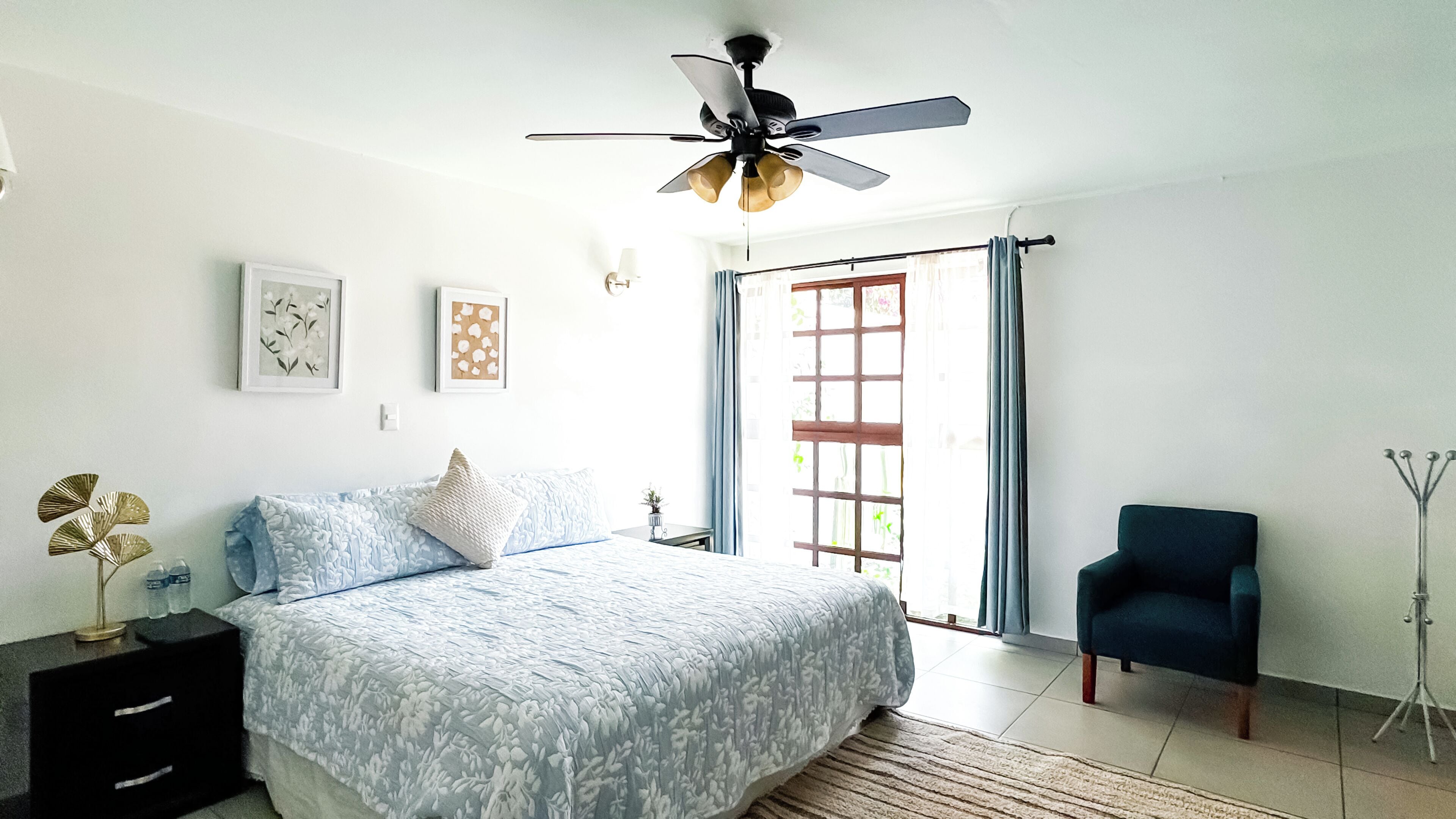 A bedroom with a bed, a desk, a chair, a ceiling fan, and a window with curtains.