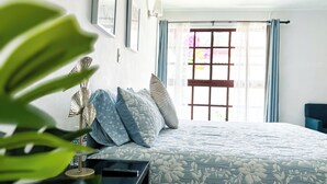 A neatly made bed with a floral-patterned bedspread, a bedside table with a remote control, and a large window with curtains. - Stylish family boutique house, 10 minutes from downtown Oaxaca. (Oaxaca City)