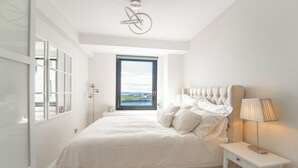 Une chambre à coucher avec un grand lit, une table de chevet avec une lampe, une fenêtre donnant sur un beau paysage et un luminaire au plafond.