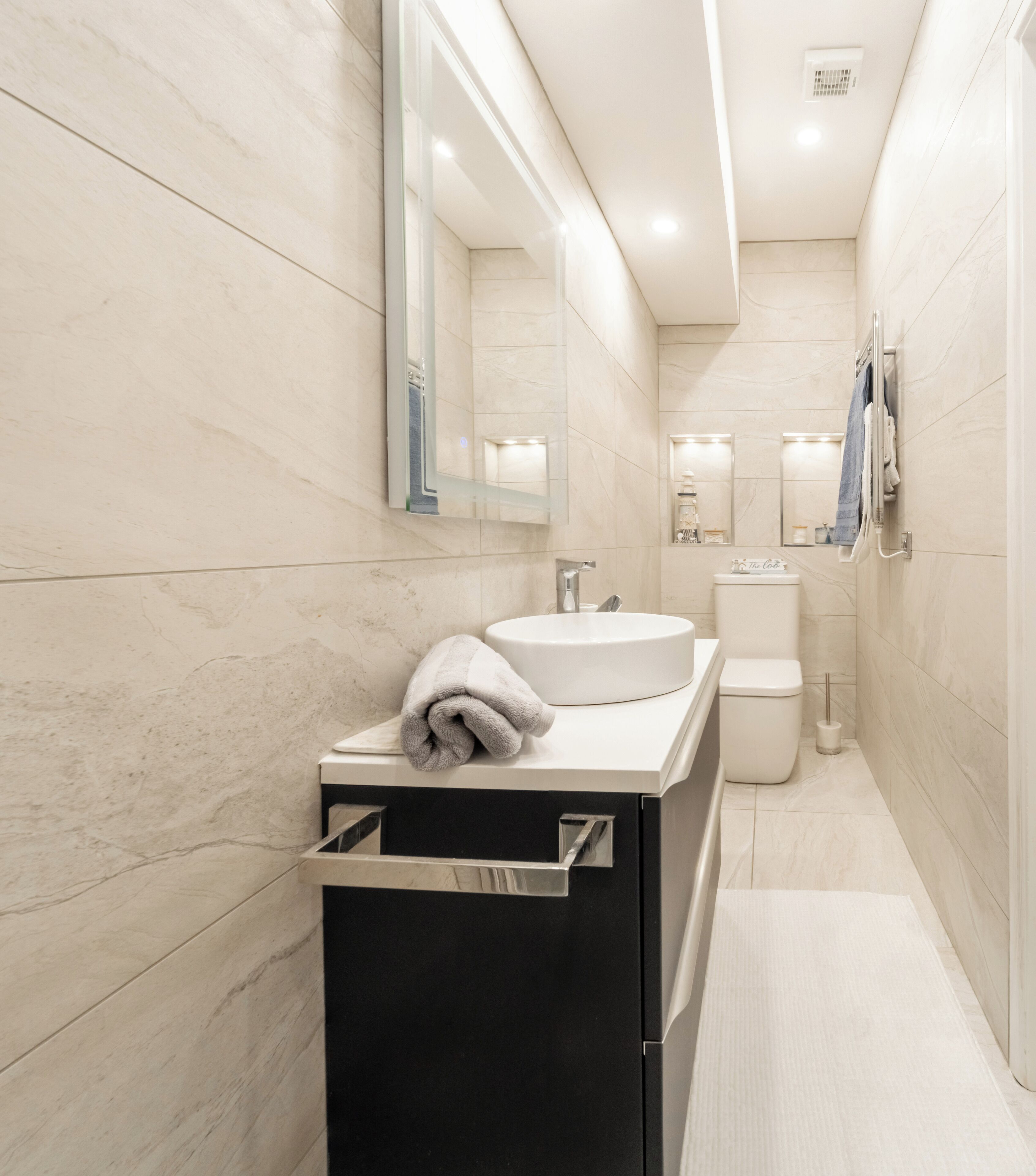 A modern bathroom with a white sink, a mirror, and a towel rack.