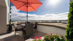 Une terrasse avec une table et des chaises, un parasol rouge et une vue sur la mer.