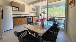 A modern kitchen with a dining area, a refrigerator, microwave, and a large window with a view of greenery. - Apt 109 - new, cozy, 150 meters from the beach, we have other apartments. (Ubatuba)