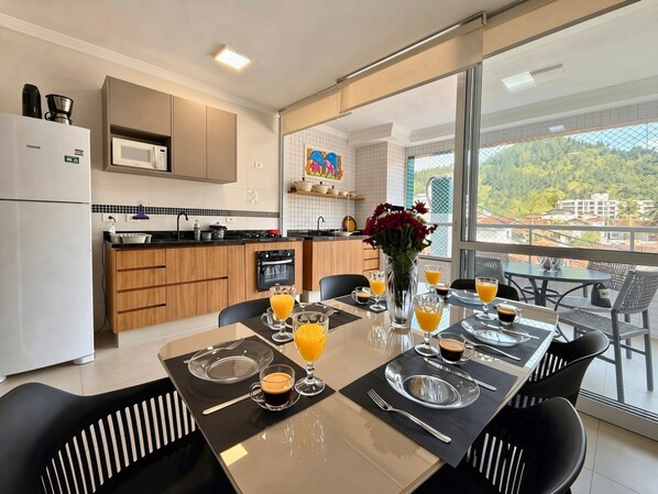 A modern kitchen with a dining area, large windows, and a view of the city. - Apartment 109—new, cozy, 150 meters from the beach; we have other apartments available. (Ubatuba)