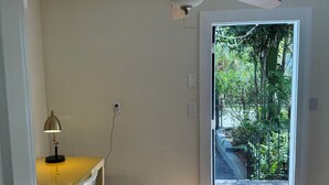 A room with a ceiling fan, a desk with a lamp, a chair, and a door leading outside.