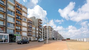 Un edificio residencial de varios pisos con balcones, una calle pavimentada y cielo despejado.