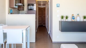 Una cocina moderna con electrodomésticos integrados, un comedor con mobiliario blanco y un pasillo que lleva a una puerta.