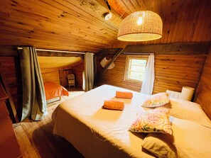 Un dormitorio de cabaña acogedor, con cama, almohadas, una ventana y una lámpara colgante.
