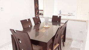 Un comedor con una mesa rectangular y seis sillas, un florero decorativo y un estante en la pared con objetos.