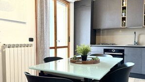 Een moderne keuken met donkere kasten, een ingebouwde oven en een eethoek met een glazen tafel en zwarte stoelen.
