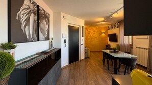 Een moderne woonkamer met een groot schilderij, een eethoek met een tafel en stoelen, en een keuken met een fornuis en een televisie.