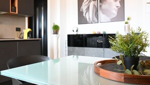 Een moderne keuken met een glazen tafel, een kamerplant en kunst aan de muur.
