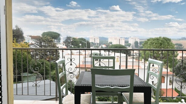 Un balcone con tavolo e sedie, vista su un paesaggio urbano con edifici e alberi.