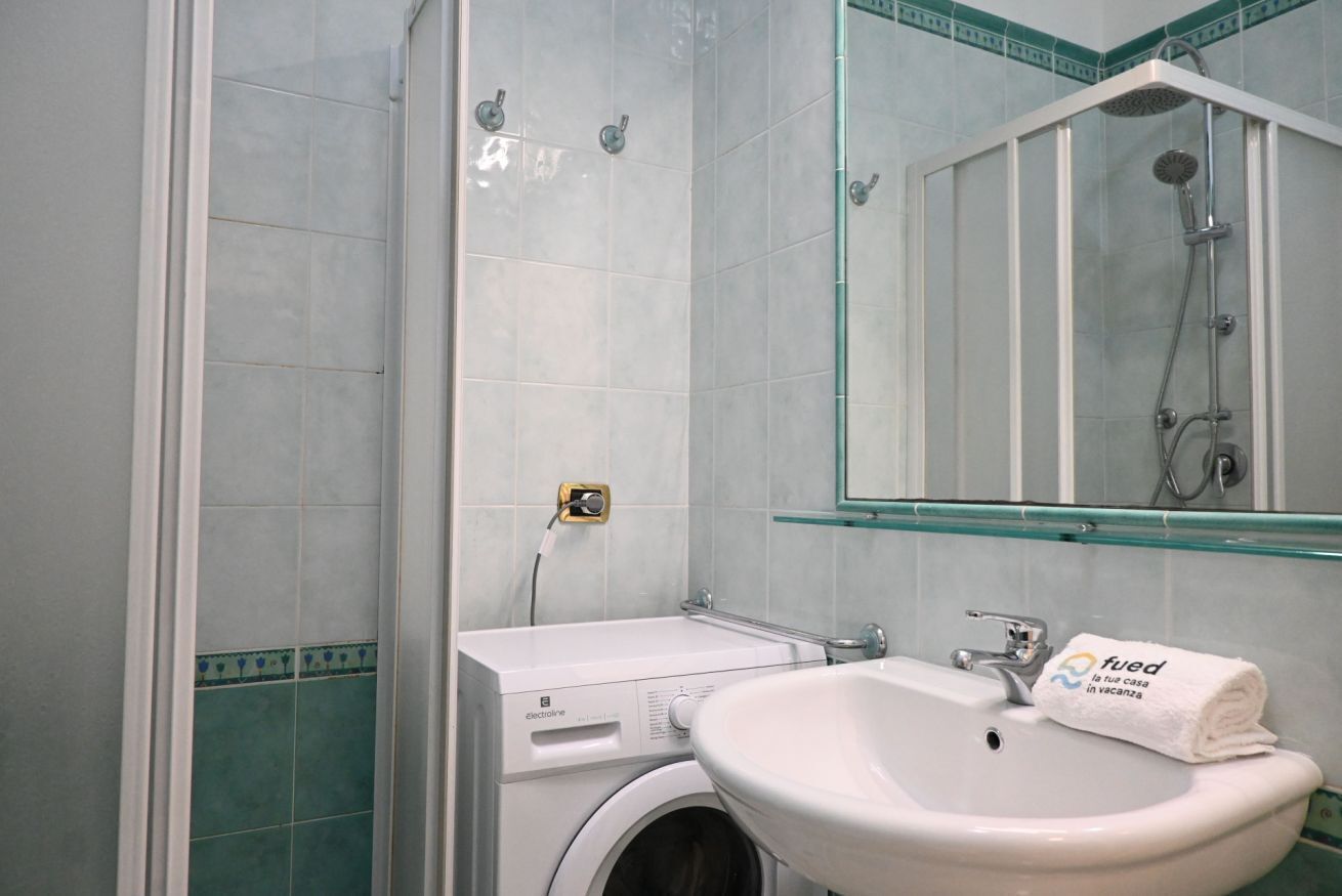 A bathroom with a glass shower enclosure, a washing machine, and a sink with a towel.