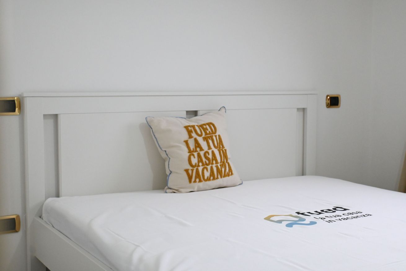 A bed with a white headboard and a pillow with text.