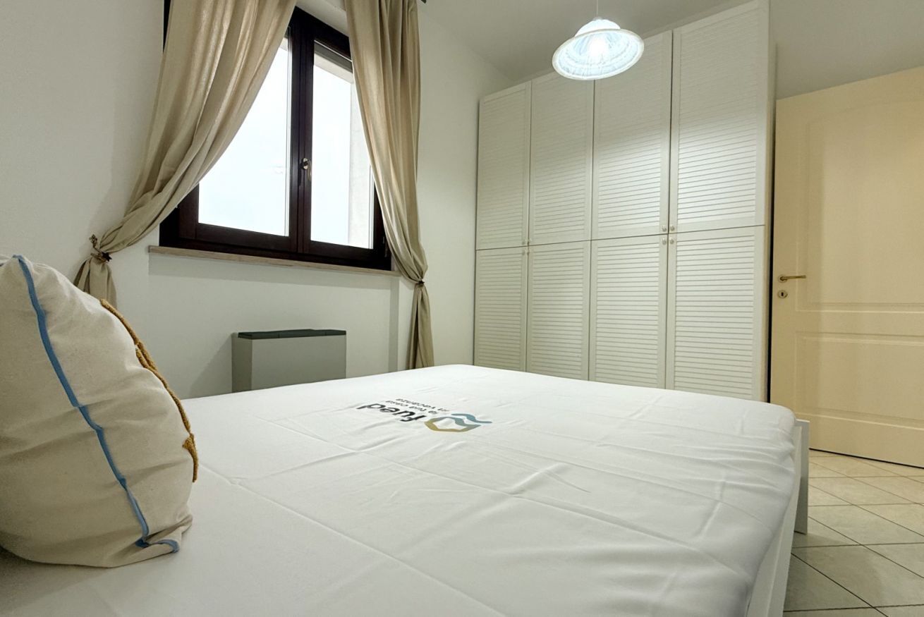 A bedroom with a bed, a window with curtains, a wardrobe, and a bedside table.