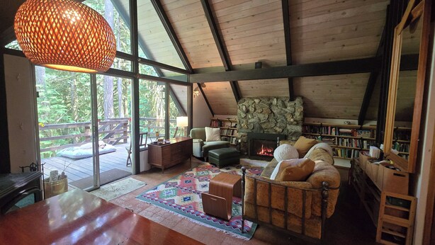 Ein gemütliches Blockhaus-Interieur mit Kamin, Bücherregalen, einer bequemen Sitzecke und großen Fenstern mit Blick auf den Wald.