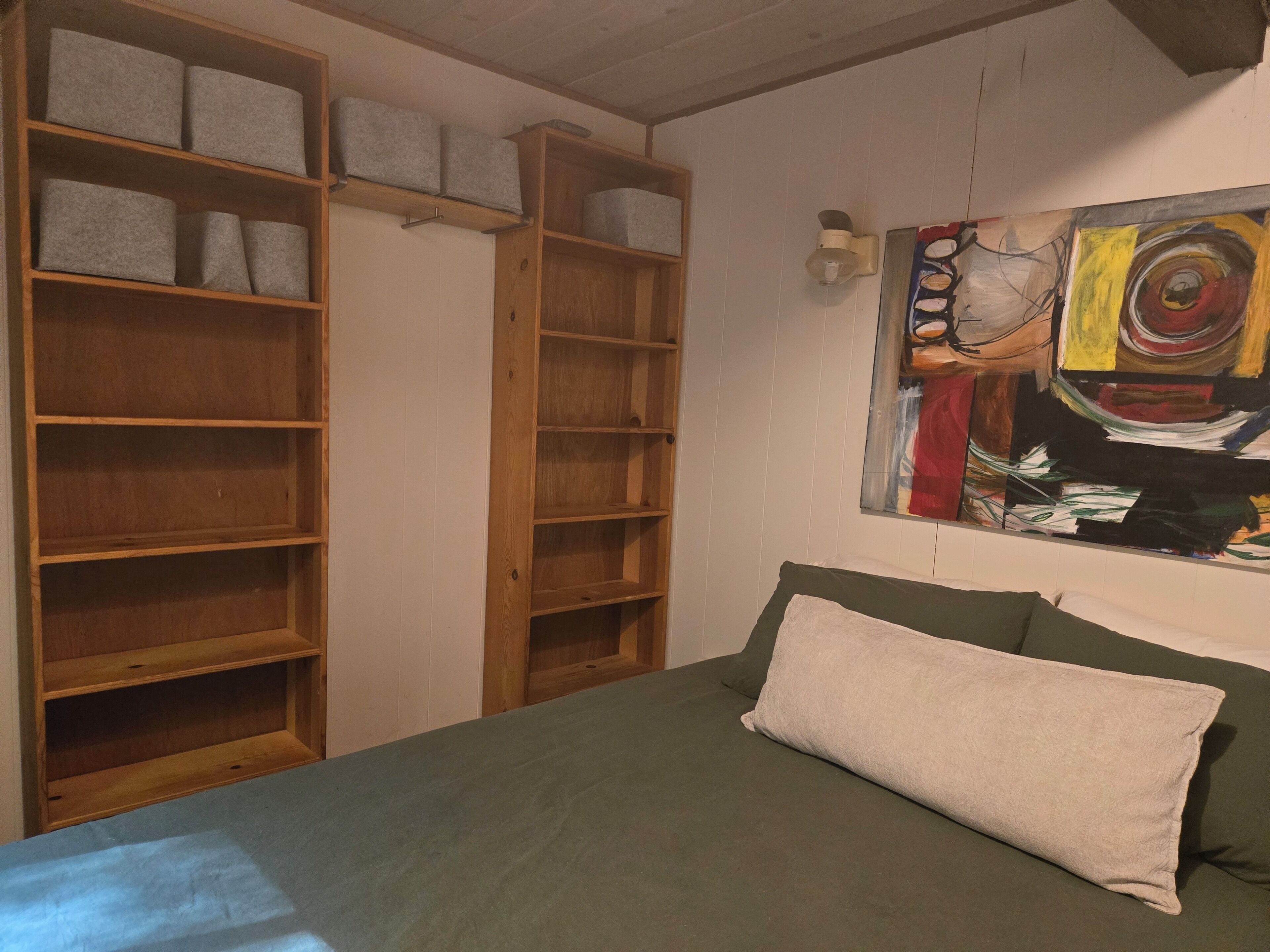 Ein Zimmer mit einem Bett, einem hölzernen Bücherregal und einem Wandbild.
