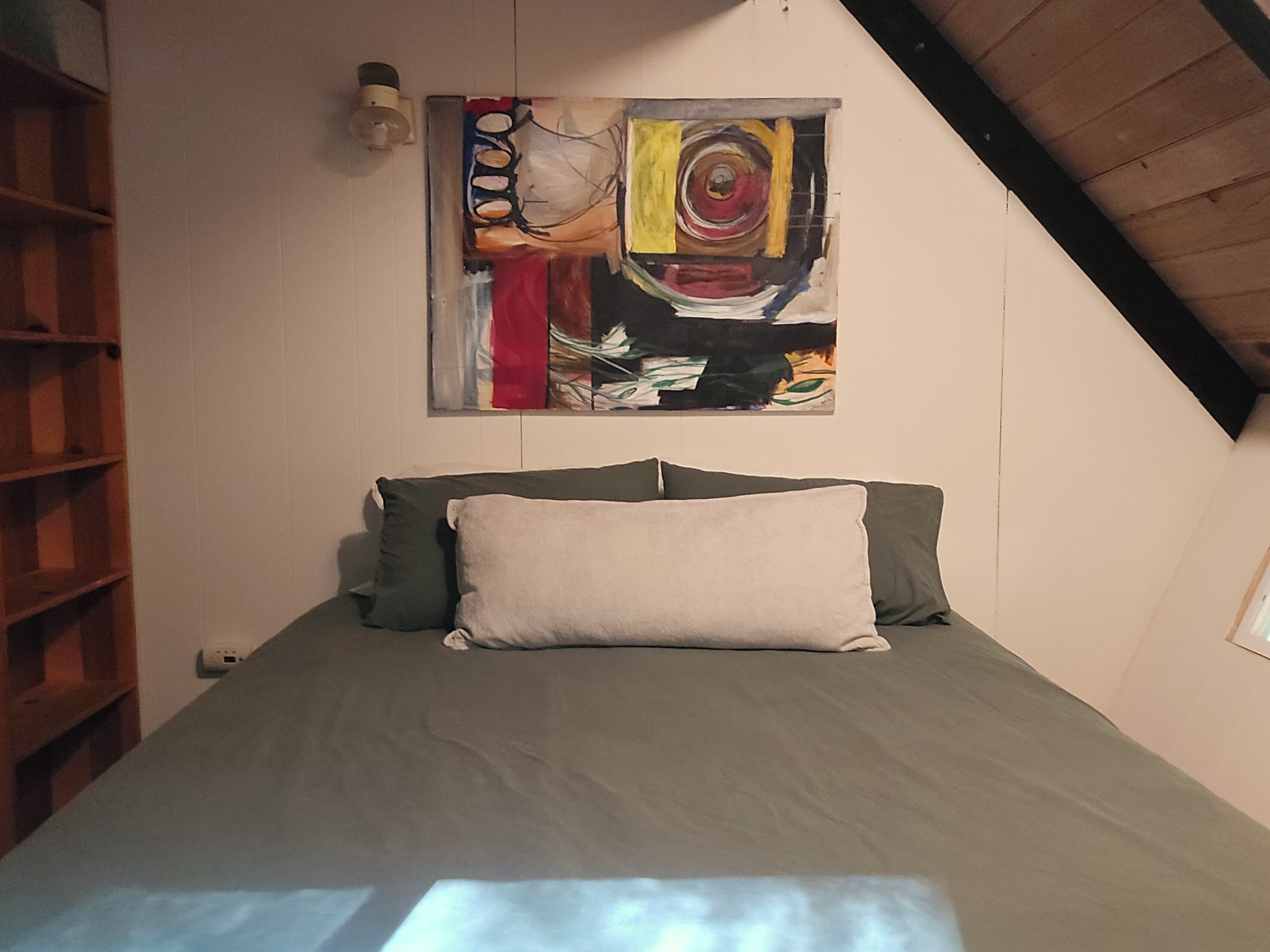 A bedroom with a bed, a painting, and a sloped ceiling.