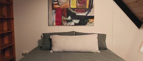 A bedroom with a bed, a painting, and a sloped ceiling.