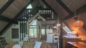 Ein Loft mit hohen Decken, einer Couch, einem Esstisch, einer Küchenzeile und einer Treppe.