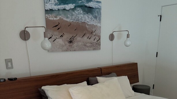 A bedroom with a large bed, a headboard, two bedside lamps, a wall-mounted artwork of a beach scene, and a door to the right. - Tremendous 3-bedroom condo with WiFi in Marina del Rey (Marina del Rey)