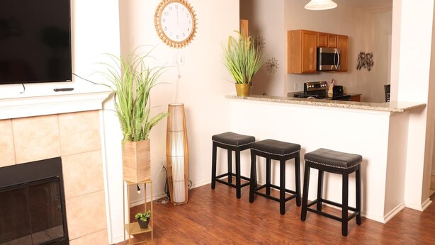 A modern kitchen with wooden cabinets, a black refrigerator, and a countertop. There are three black stools with metal legs and a potted plant on the counter. - Work Play Stay Pet-friendly With Foosball (Aubrey)