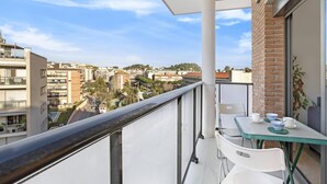 Un balcón con mesa y sillas, con vista a un paisaje urbano con edificios y árboles.