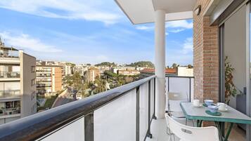 A balcony with a table and chairs, overlooking a cityscape with buildings and trees.