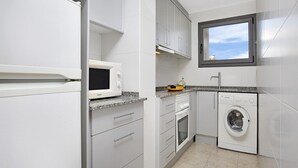Cocina compacta con armarios blancos, microondas, lavadora y ventana sobre el fregadero.